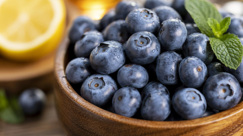 Close-up of fresh blueberries in a wooden bowl with a sprig of mint