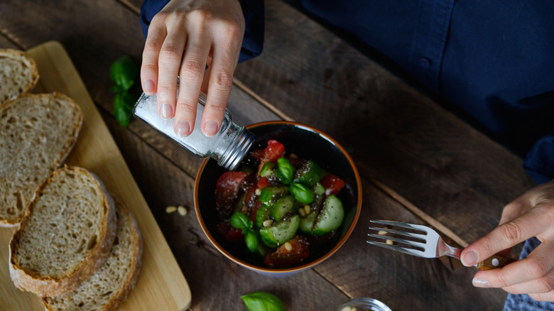 Person pouring salt on bowl of veggies