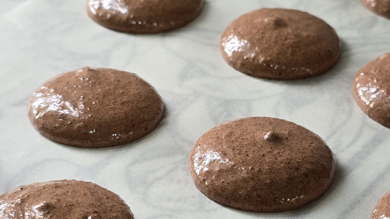 a close up of piped chocolate macaron shells