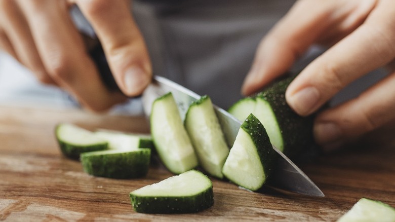 Hands chop cucumber on a wooden cutting board