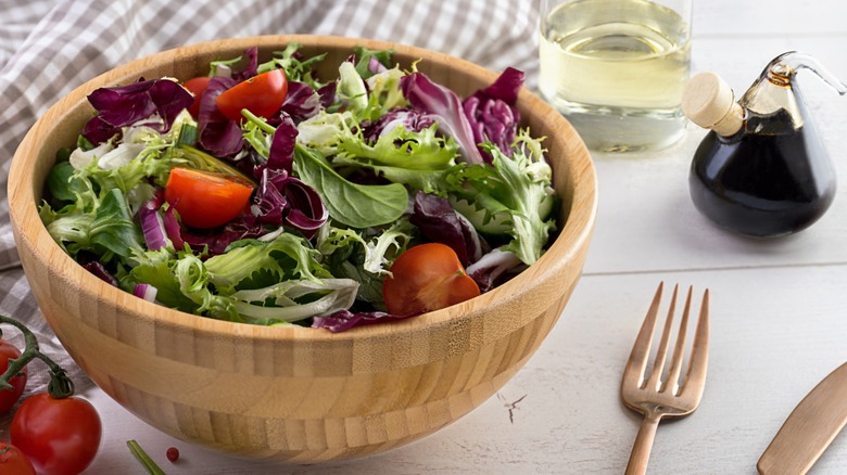 A wooden bowl of store-bought salad mix with tomatoes