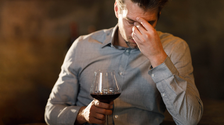 A man having a headache while drinking wine in a bar.
