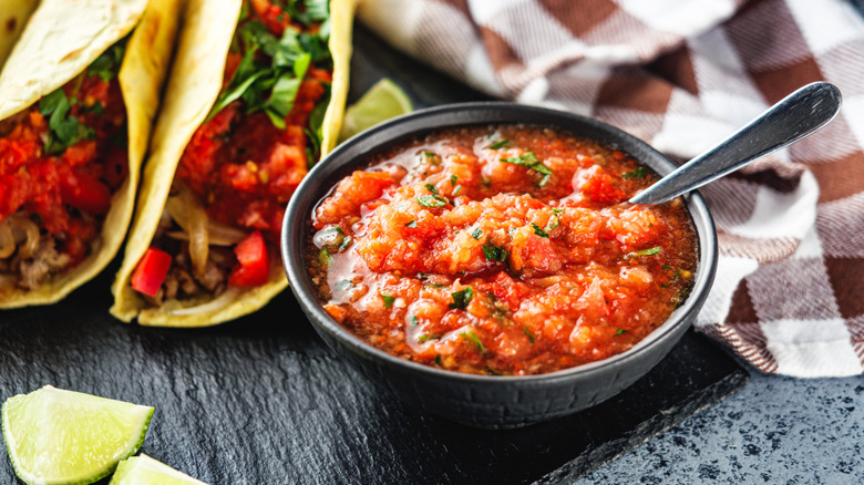 A bowl of salsa next to tacos on a black table