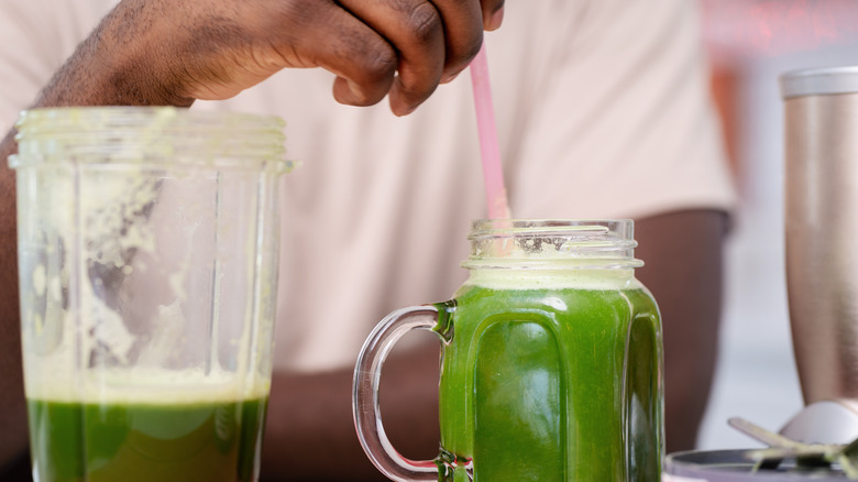 a person stirs a glass of green juice
