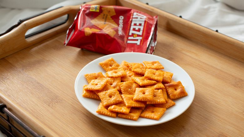 White plate of Cheez-Its with open snack-size bag on wood serving tray.