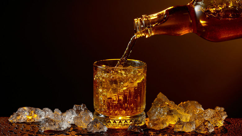 a bottle of whiskey being poured into a fancy glass surrounded by crushed ice