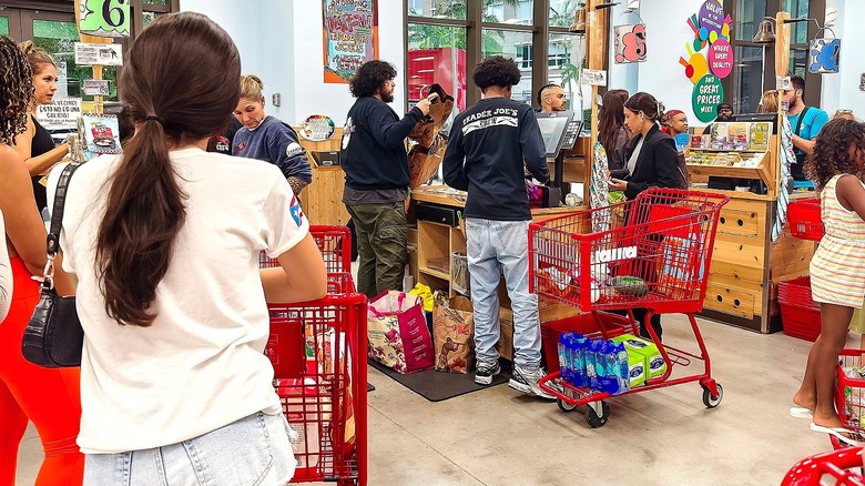 Customers waiting and employees unloading groceries in the checkout area at Trader Joe's.
