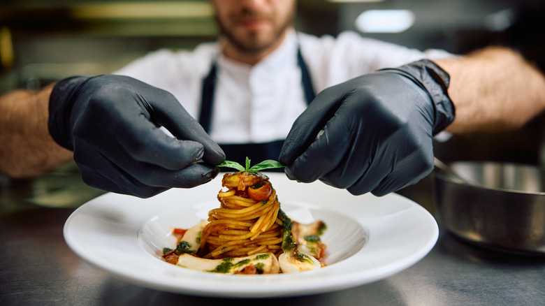 Close up of professional chef serving pasta while working in the kitchen.