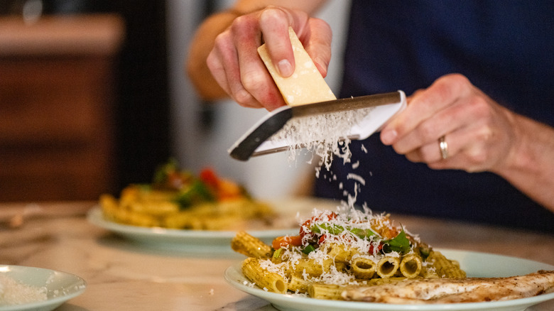 hands grating a block of Parmesan cheese over a homemade pasta dinner.