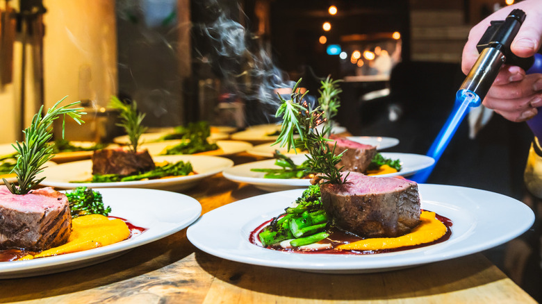 a fine dining chef preparing steak with a torch