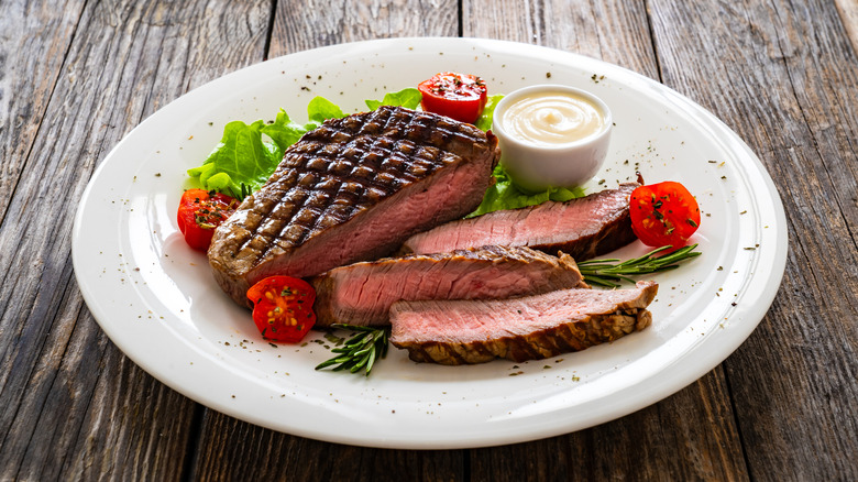 Sliced grilled sirloin steak on a white plate with vegetables