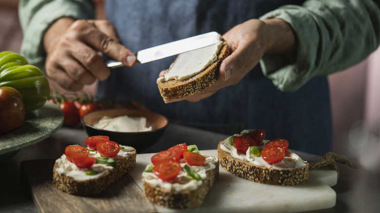 a plain tomato and mayo sandwich on brown bread on a white plate with a wooden chopping board with sliced tomatoes in the background
