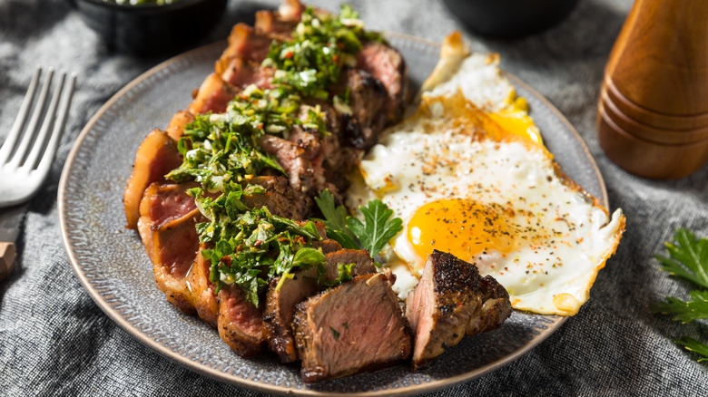 A plate of steak and eggs with chimichurri on top.