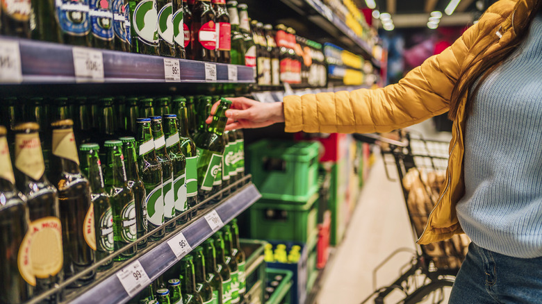 A hand picking out a beer at a grocery store