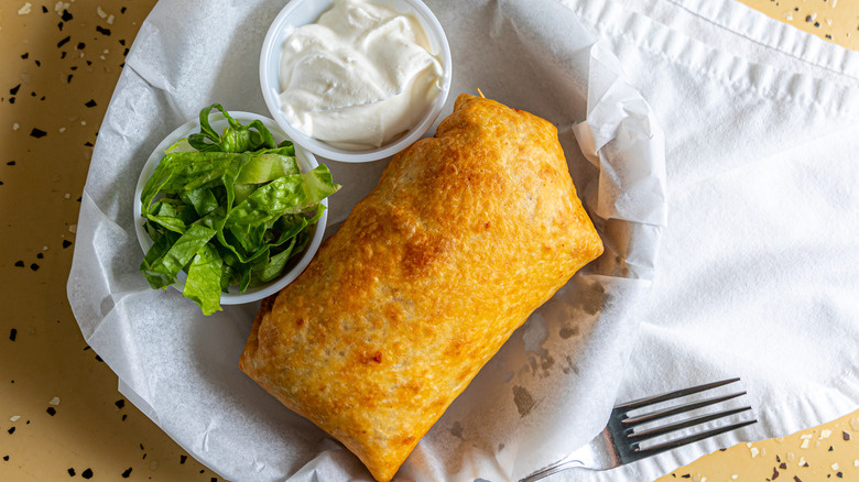 Fried burrito in a basket with small plastic cups of sour cream and lettuce