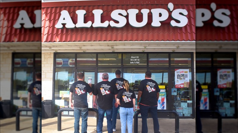 Group of people standing in front of an Allsup's and facing away from the camera wearing fried burrito T-shirts
