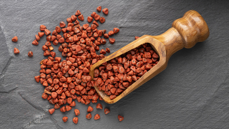 A scoop of achiote seeds on a table.