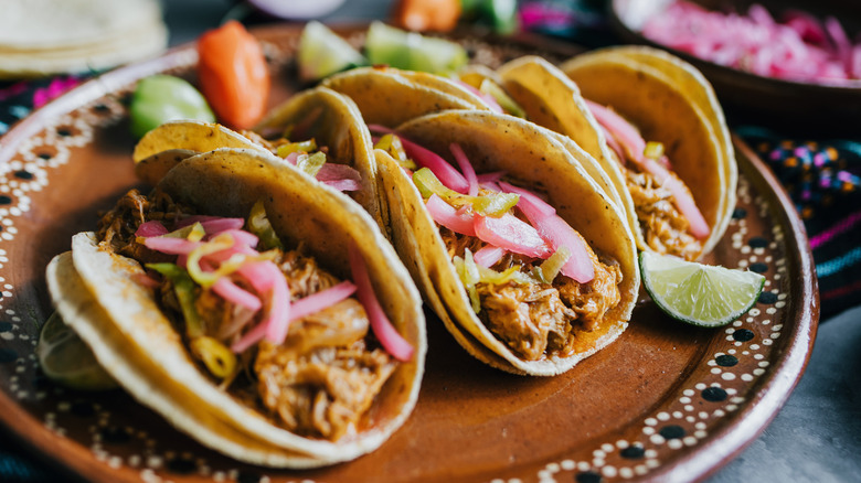3 cochinita pibil tacos on a wooden platter.