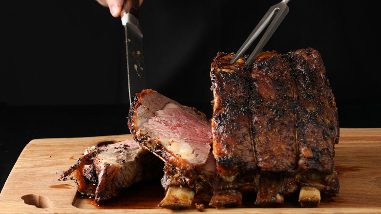 A chef slicing a prime rib roast on a wooden cutting board.