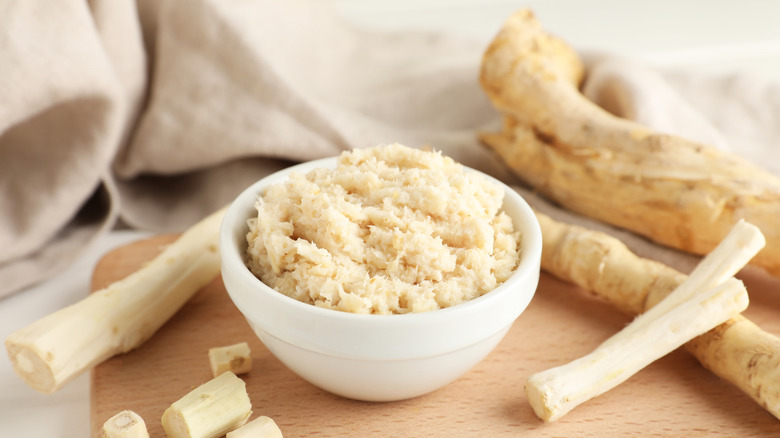 A bowl of horseradish surrounded by fresh horseradish roots