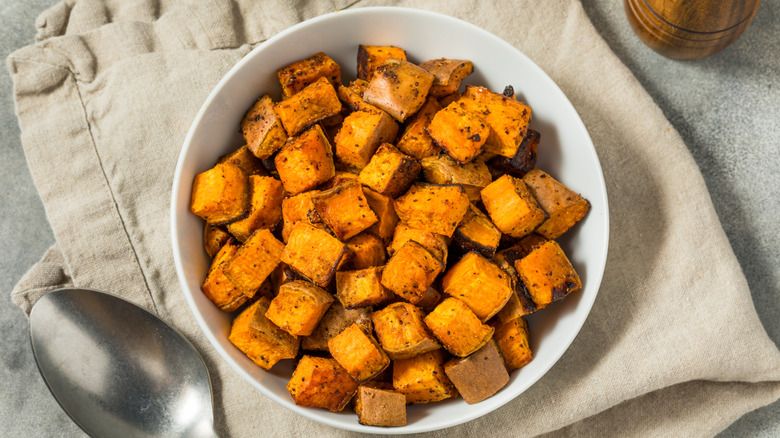 A white bowl of roasted sweet potatoes on cloth towel.