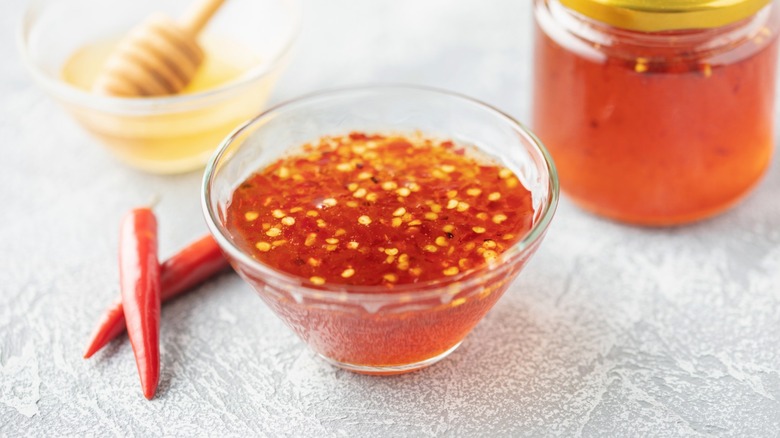 A small glass bowl of homemade hot honey with jar in the background.