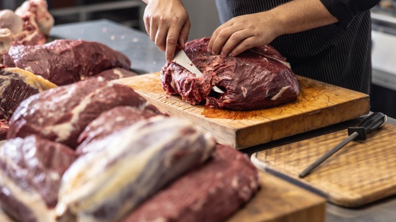 A person cutting raw beef in a commercial restaurant kitchen.