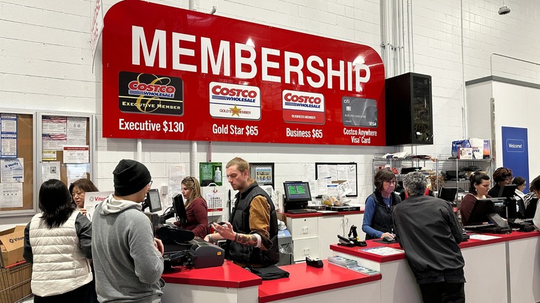 A busy Costco membership service counter displaying the prices of different membership tiers