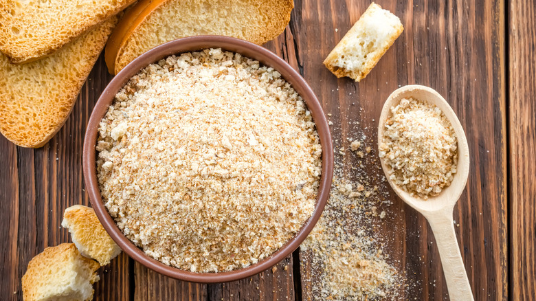 A bowl and a spoonful of breadcrumbs arranged around sliced bread.