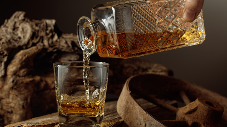 An individual pouring whiskey into a glass.