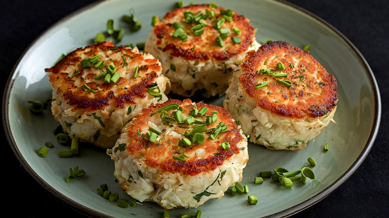 Four crab cakes on a plate with green onion garnish.