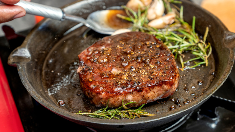 Cooking steak in a pan with rosemary and garlic