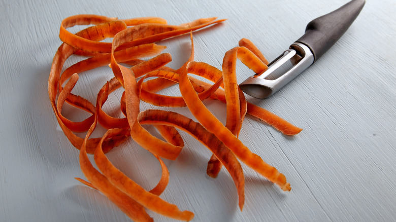 An illustrative image showing carrot peels on a light wooden table with a peeler.