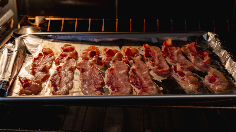 Bacon slices cooking in the oven on a foil-covered tray