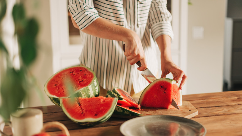 A woman cutting a watermelon into pieces.