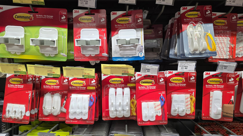 Various 3M Command adhesive hooks and wall organizers are neatly displayed on retail shelves. These no-nail, damage-free hanging solutions are commonly used in homes.