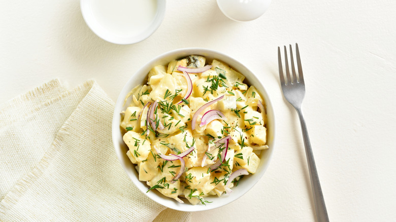 Potato salad with fresh ingredients on white table