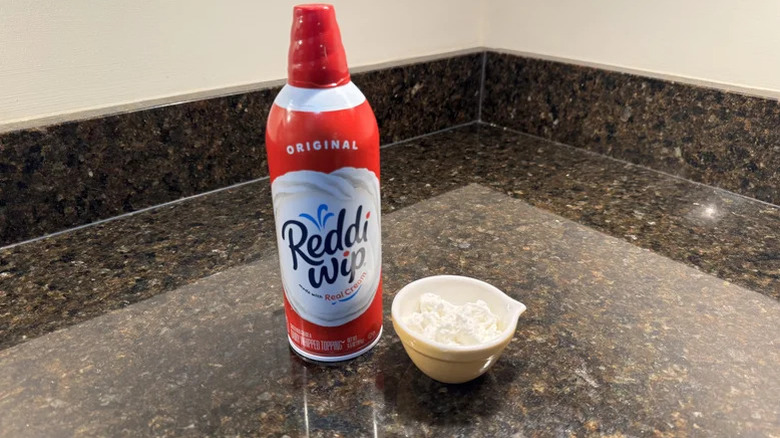 A can of Reddi-wip next to a bowl of it on a kitchen counter.