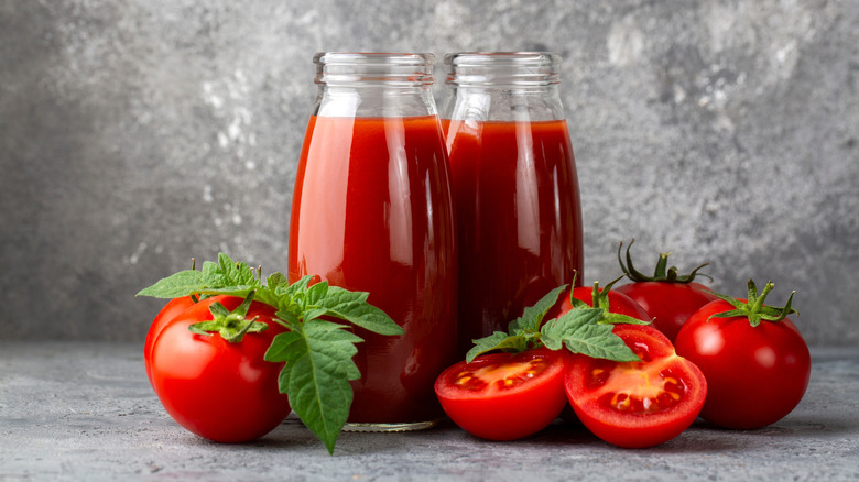 Glass bottles of tomato juice with whole and halved tomatoes