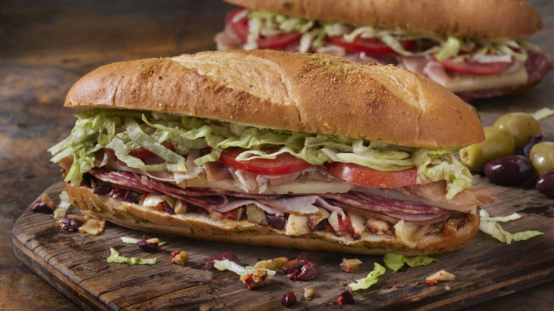two sub sandwiches with meat and veggies on a wooden board