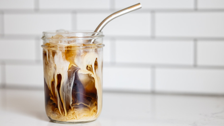 Iced coffee in a glass sitting on a white table with a metal straw