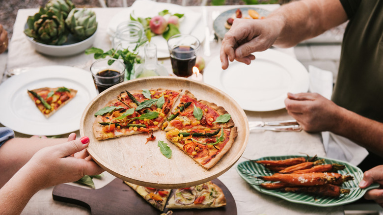 Person passing plate of vegan pizza across table