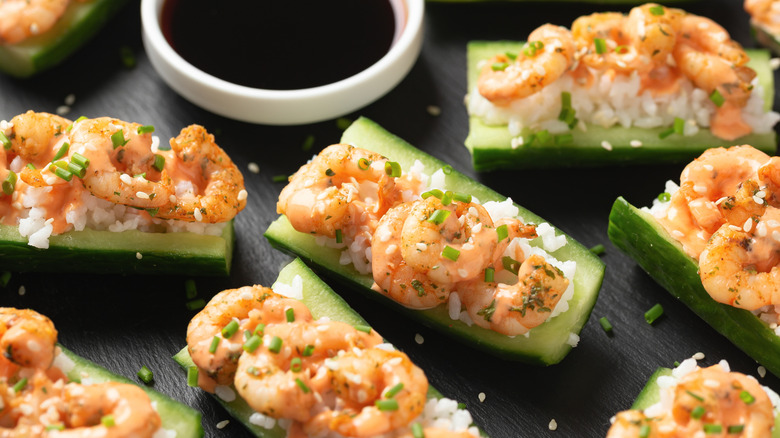 Cucumber sushi boats with rice, shrimp, and green onions next to a dish of soy sauce