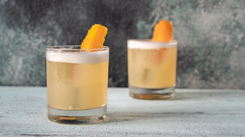 Two whiskey sours with orange peel garnish