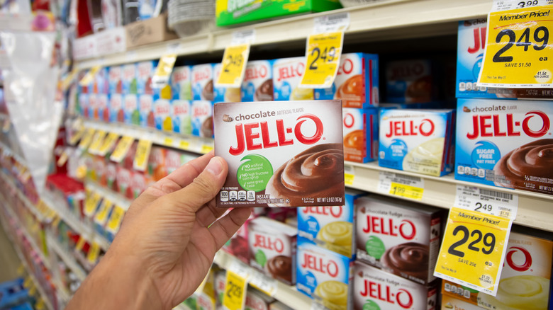 Hand of a grocery store shopper holding pack of chocolate Jell-O pudding