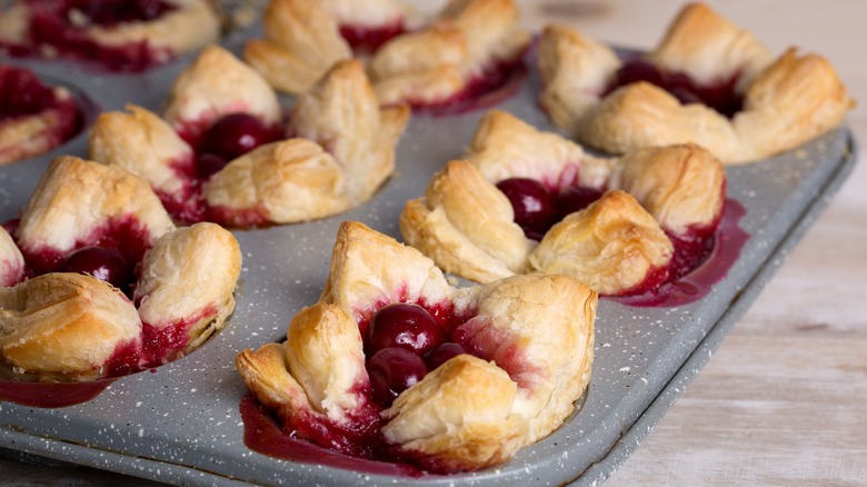 Cherry pie puff pastries in muffin tin, on top of wood counter.