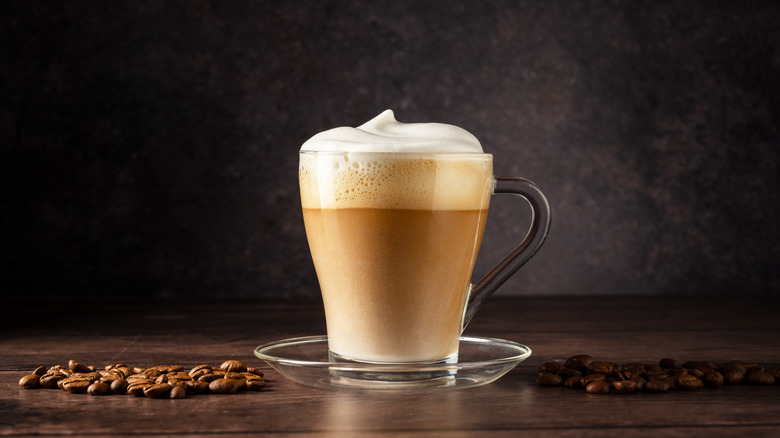 A hot latte in a glass cup with coffee beans on the side