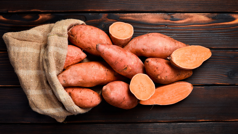 A bunch of raw sweet potatoes spilling out from a burlap bag, placed on a wooden floor