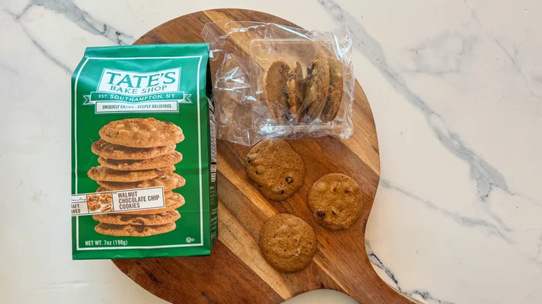 A pack of Tate's Bake Shop walnut chocolate chip cookies on a wooden board, with some of the cookies sitting next to the package.