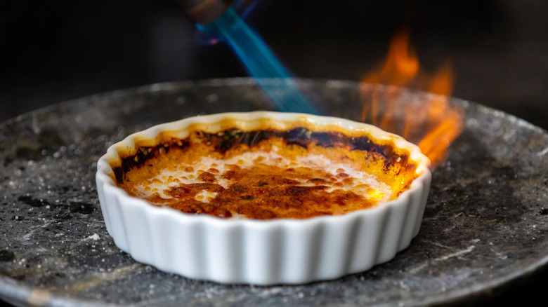 A torch's blue and orange flame is seen firing the surface of a crème brûlée.